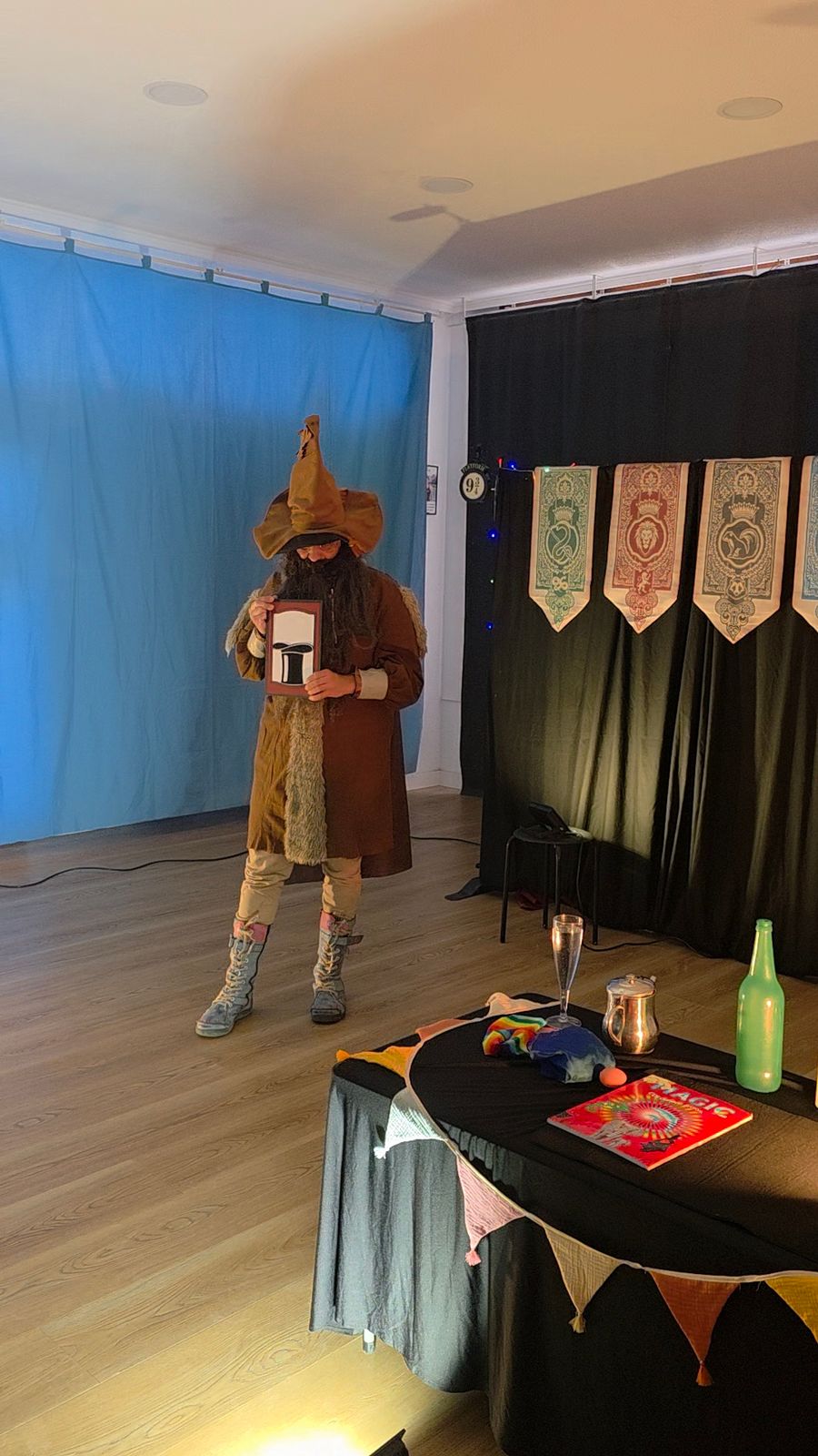Mago disfrazado con sombrero y capa durante la función de la Escuela de Magia, con su mesa de trucos en primer plano