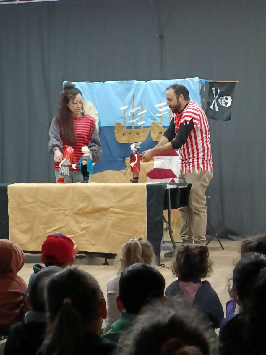 Dos titiriteros representando una función de piratas con marionetas ante un grupo de escolares sentados en el suelo